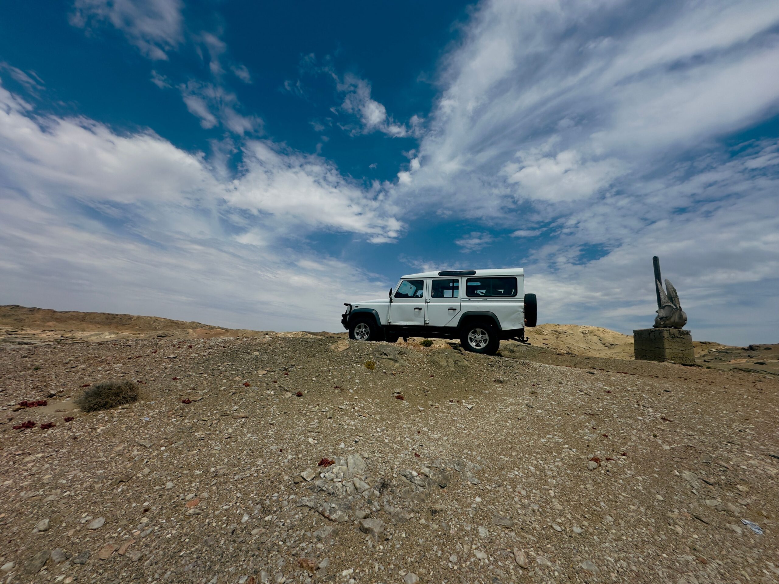 Un véhicule 4x4 garé sur un terrain rocailleux près de Luderitz, en Namibie, à côté d’un monument en pierre