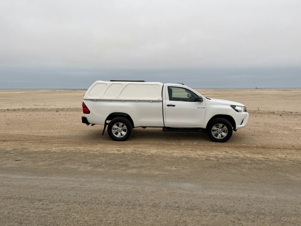 White self-drive pickup truck parked in a remote Namibian desert landscape